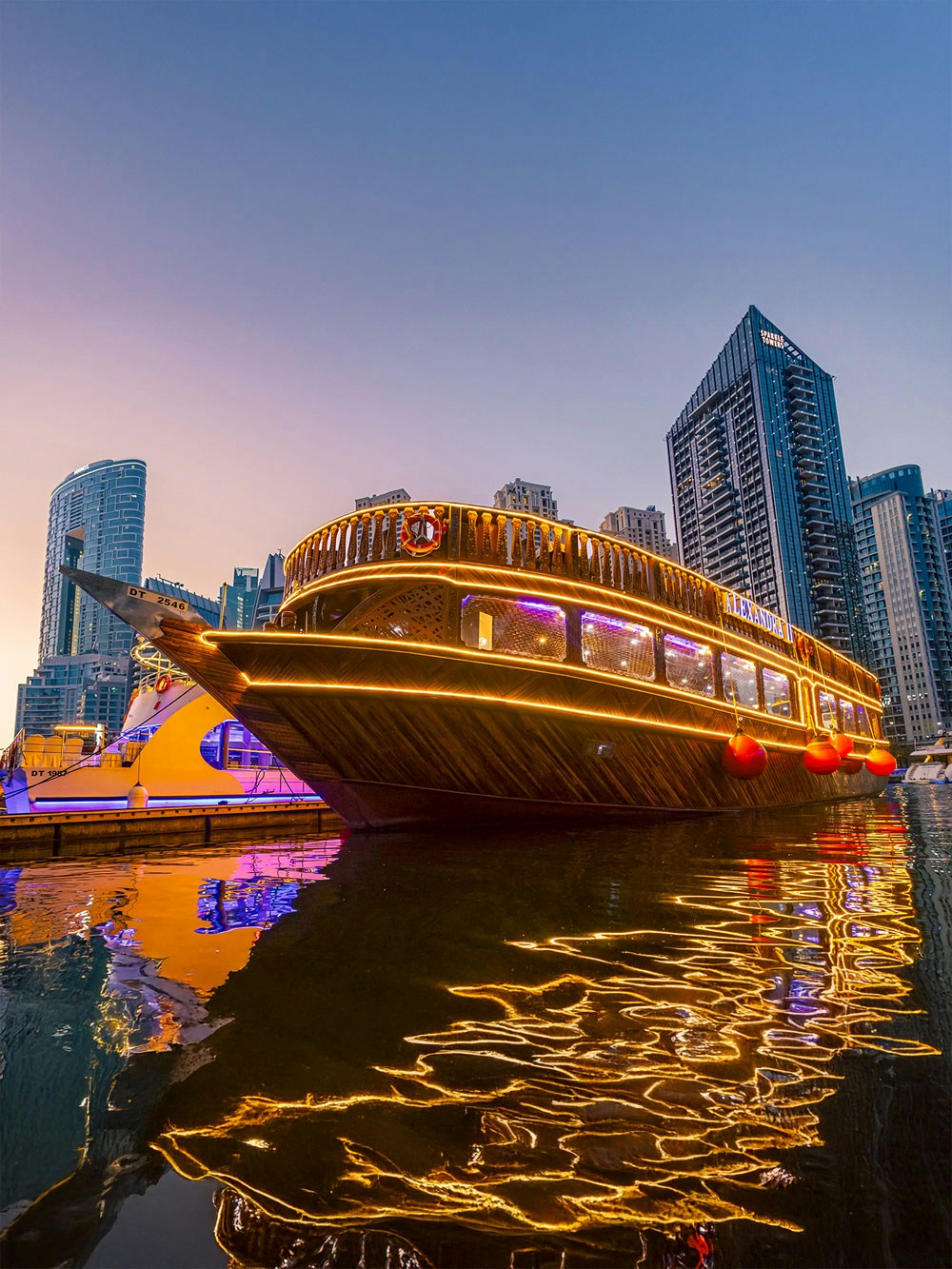 Alexandra Dhow Cruise illuminated at Dubai Marina during sunset.