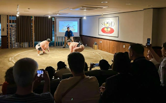 Sumo wrestlers preparing for a match in a Tokyo arena with an audience watching.