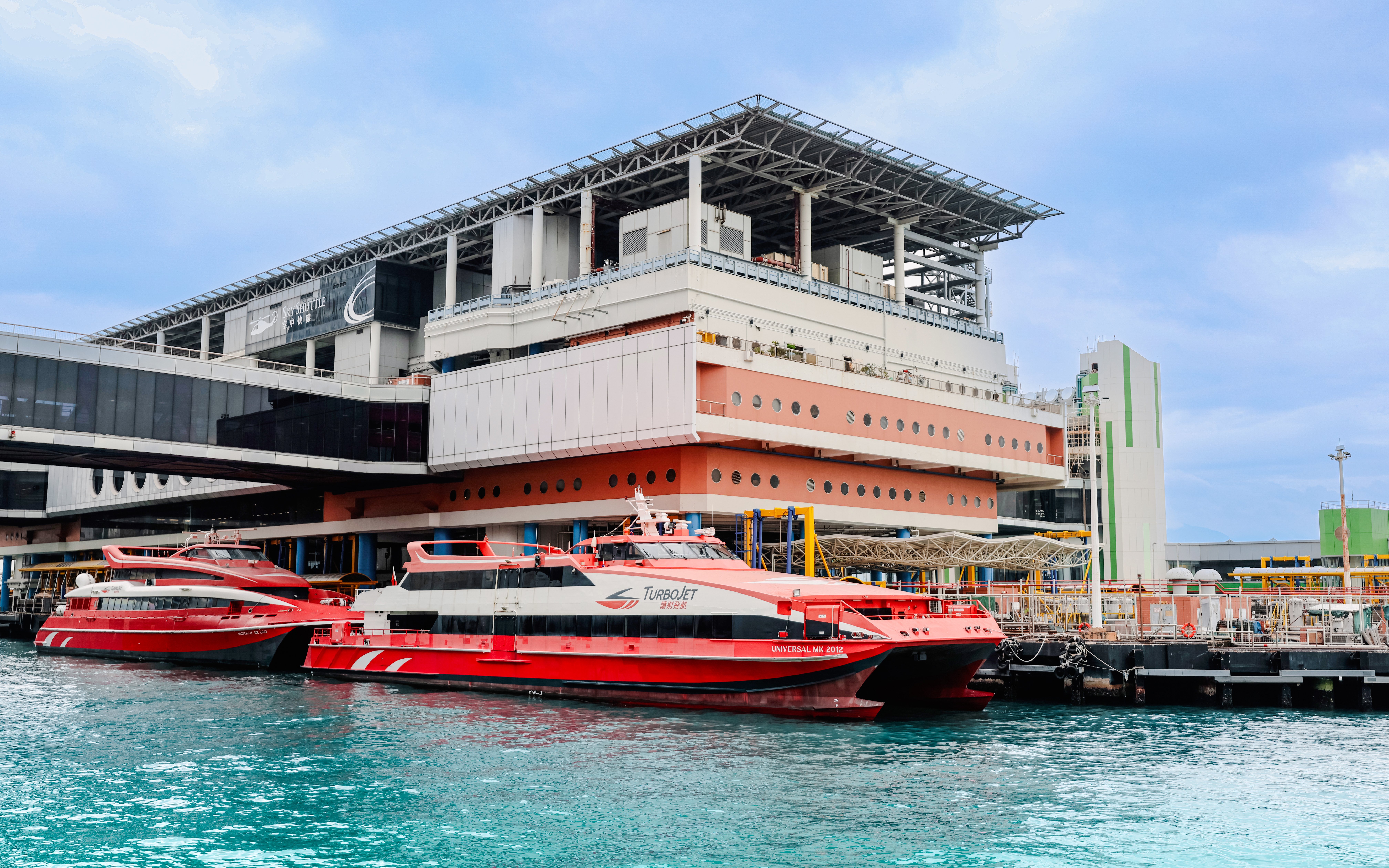 Ferry terminal in Hong Kong with red ferries docked, cloudy sky above.