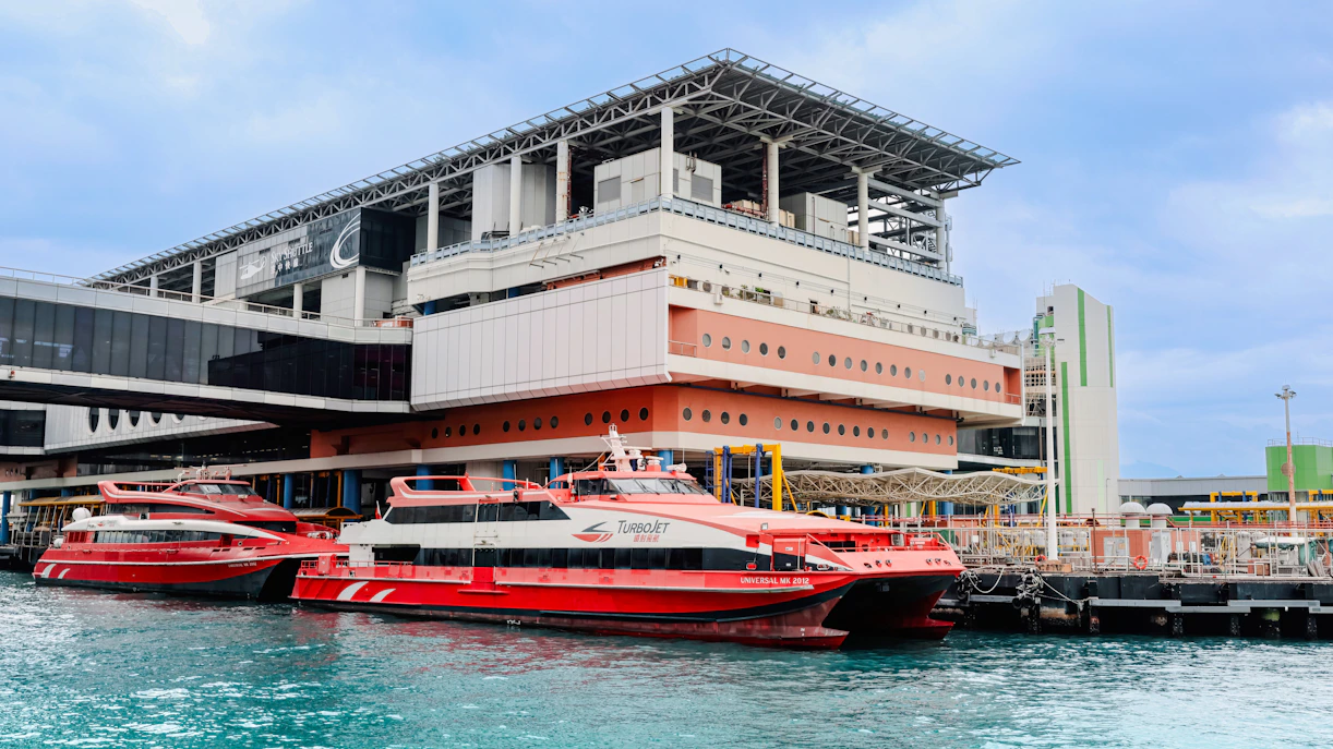 Ferry terminal in Hong Kong with red ferries docked, cloudy sky above.