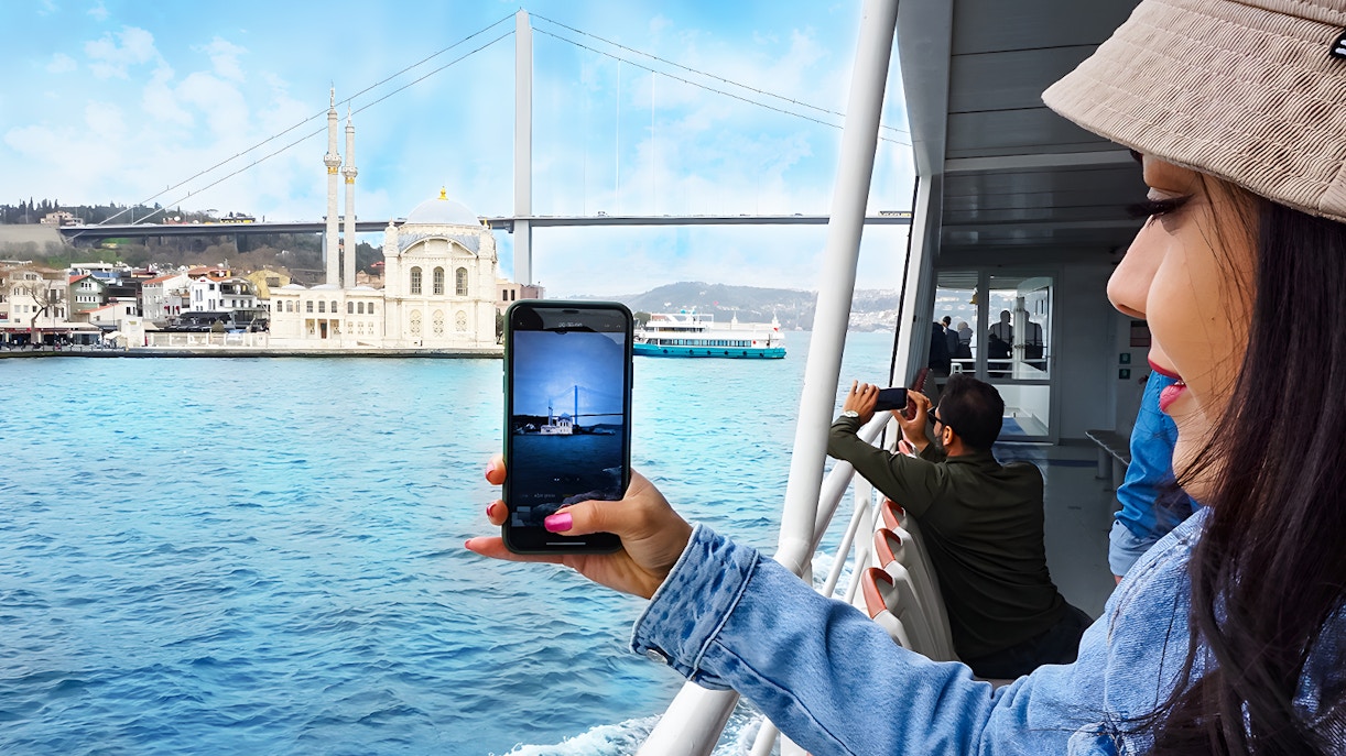 Bosphorus cruise passengers photographing Ortaköy Mosque and Bosphorus Bridge in Istanbul.