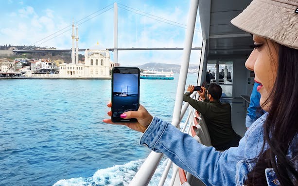 Bosphorus cruise passengers photographing Ortaköy Mosque and Bosphorus Bridge in Istanbul.
