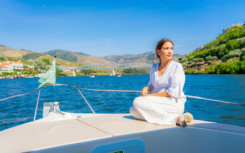 Tourist on boat enjoying Douro Valley scenery with bridge and hills in background.