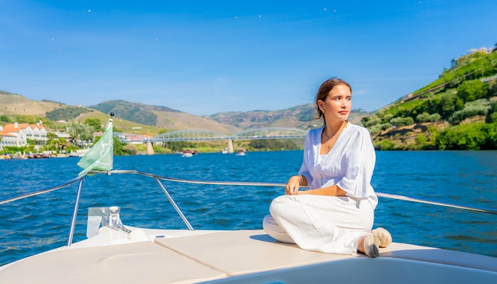Tourist on boat enjoying Douro Valley scenery with bridge and hills in background.