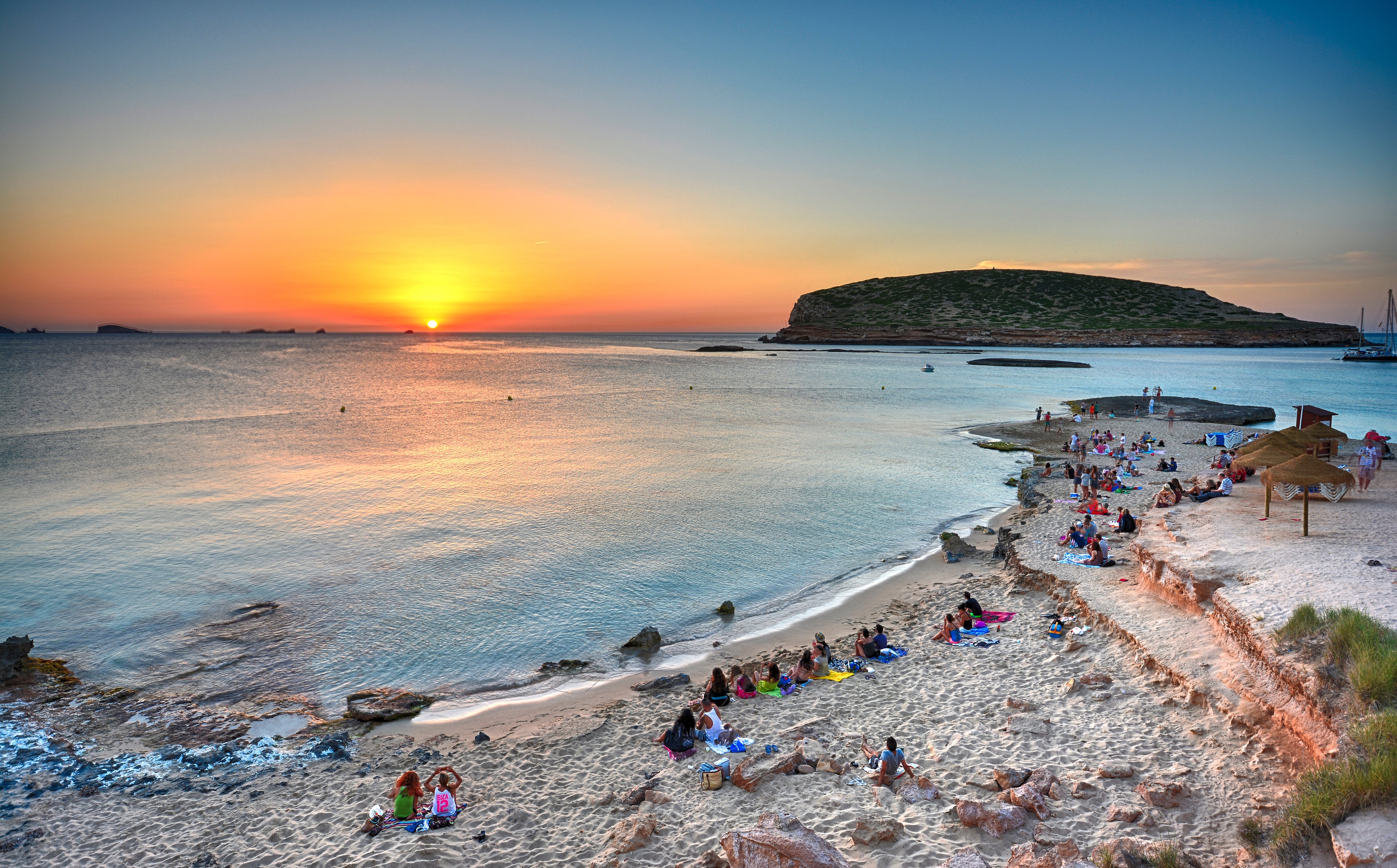 Sunset view over Cala Comte beach in Ibiza with people relaxing on the sand.