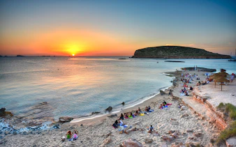 Sunset view over Cala Comte beach in Ibiza with people relaxing on the sand.
