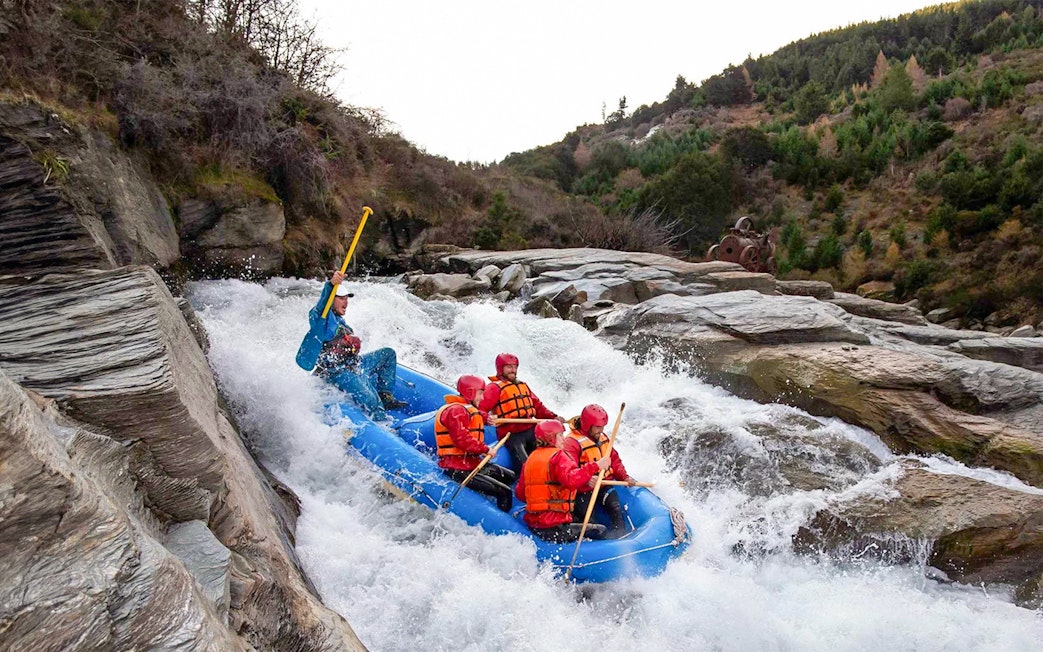Whitewater rafting on Shotover River, Queenstown, with a group navigating rapids in a blue raft.