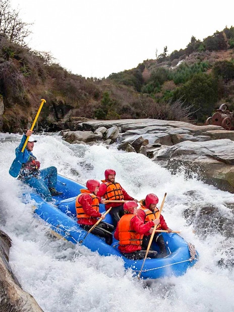 Whitewater rafting on Shotover River, Queenstown, with a group navigating rapids in a blue raft.