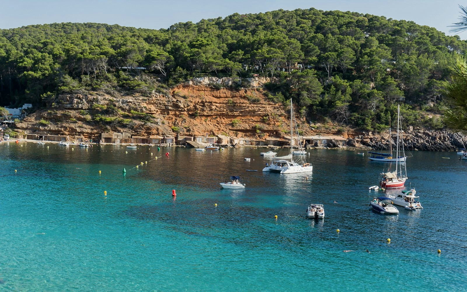 Boats anchored in the clear waters of Cala Salada beach near San Antonio, Ibiza.