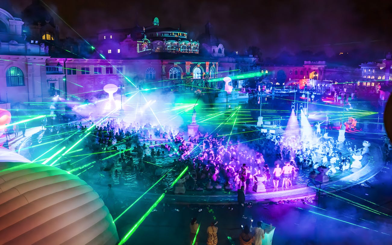 Crowd enjoying Sparty bath party with laser lights at Széchenyi Thermal Bath, Budapest.
