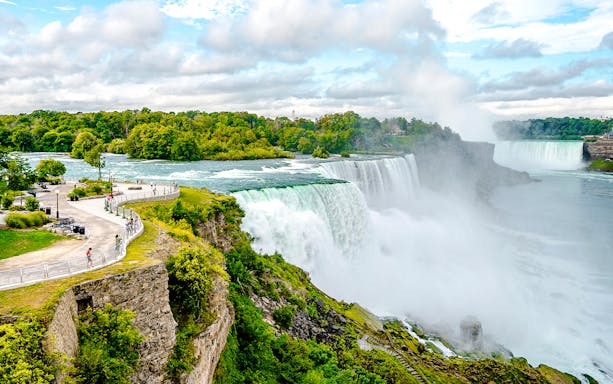 Niagara Falls USA with tourists on a viewing platform overlooking the cascading waterfalls.