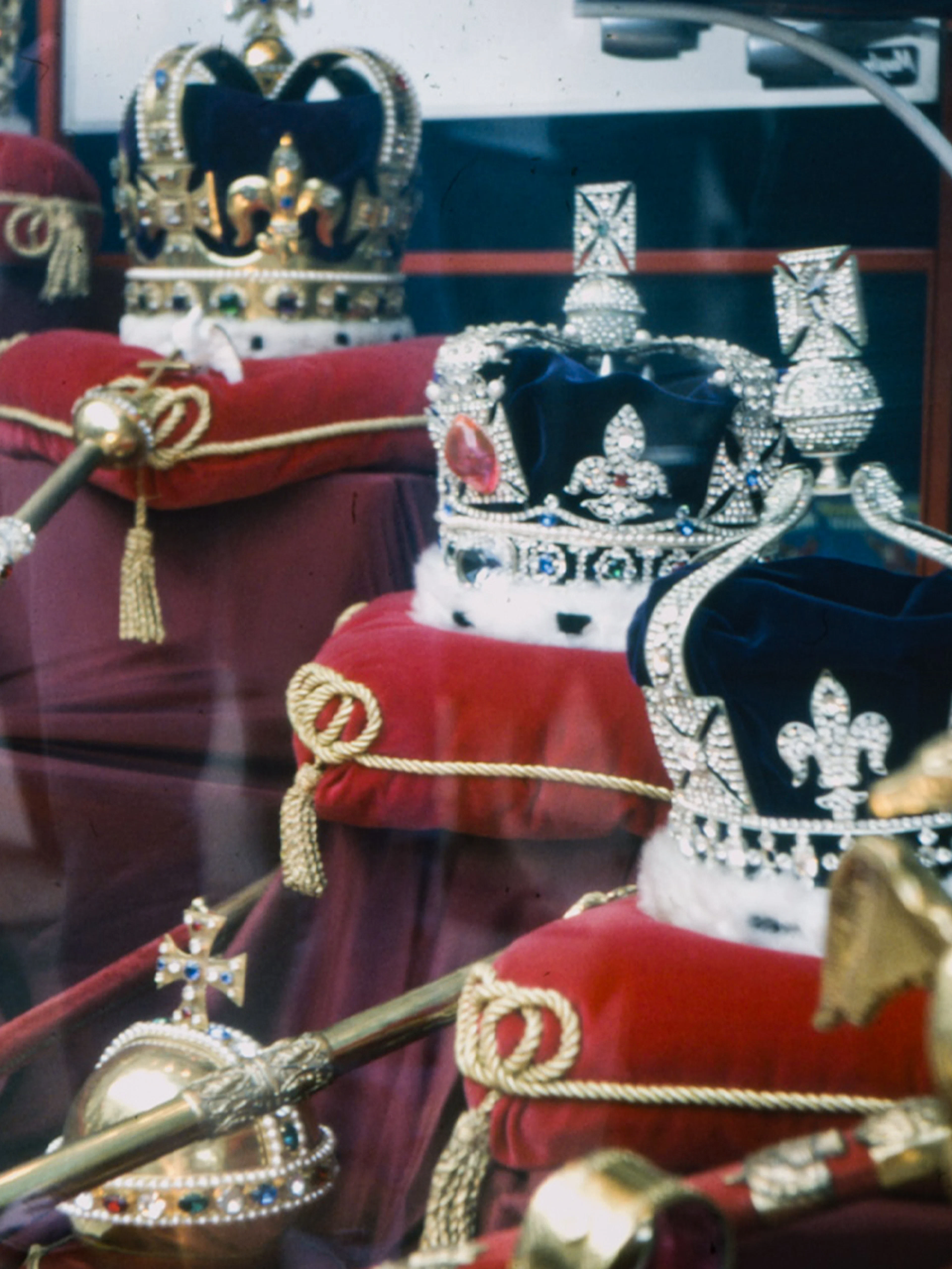 Crown Jewels display in London with crowns and scepters on red cushions.