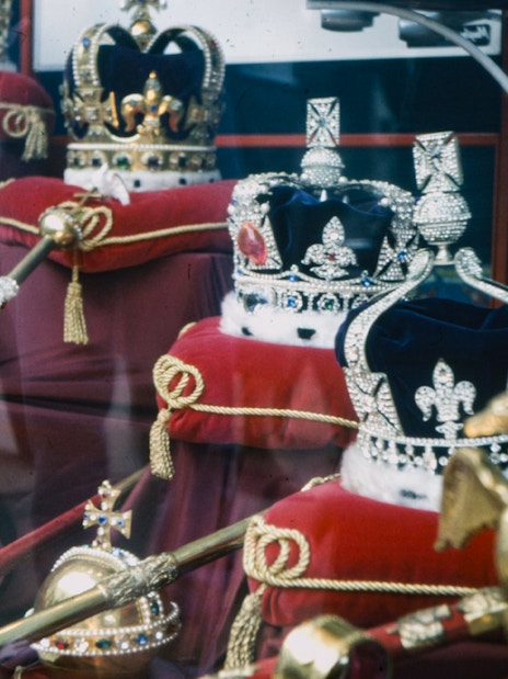 Crown Jewels display in London with crowns and scepters on red cushions.