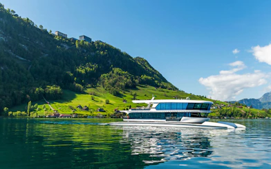 Catamaran cruising on Lake Lucerne with green hills and clear sky in the background.