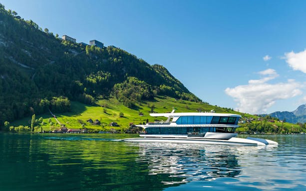 Catamaran cruising on Lake Lucerne with green hills and clear sky in the background.