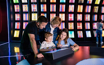 Family exploring interactive exhibit at Camp Nou Barca Museum with football jerseys in background.