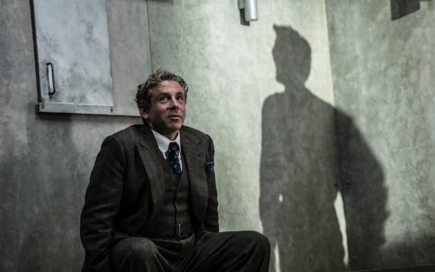 Man in a suit sitting against a wall with a shadow cast beside him.