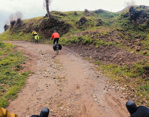 Cyclists on a dirt path in Montjuïc Park Circuit, surrounded by green hills.