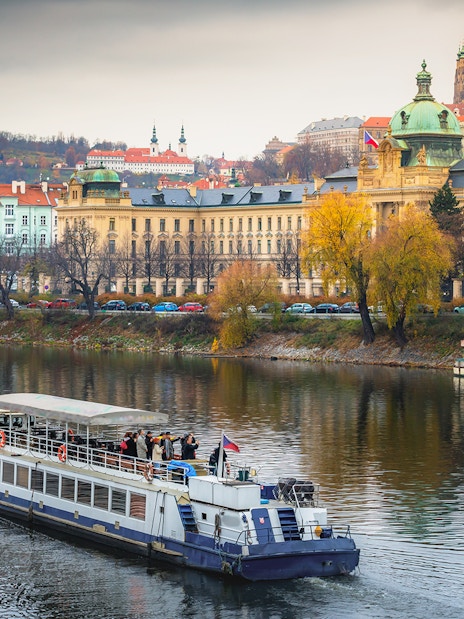 Cruise boat on Vltava River with Prague's historic buildings in the background.