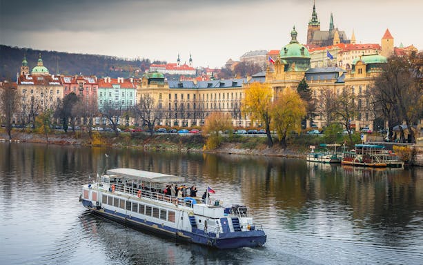 Cruise boat on Vltava River with Prague's historic buildings in the background.