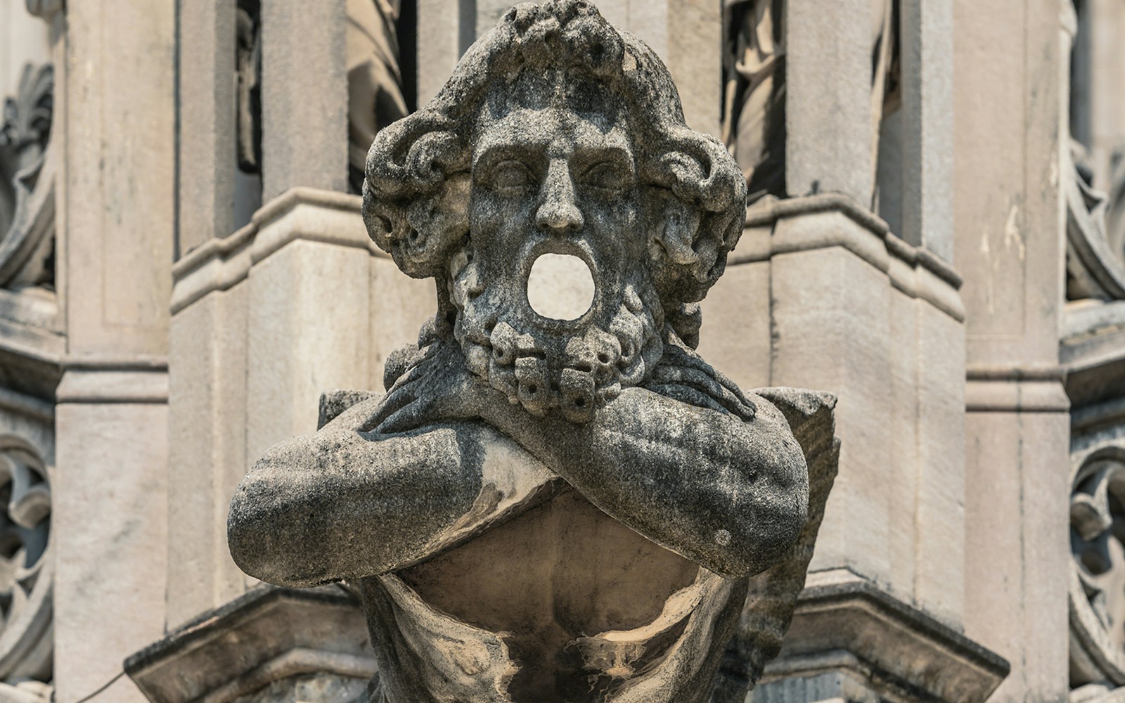 Stone statue with open mouth on Milan Duomo Cathedral exterior.
