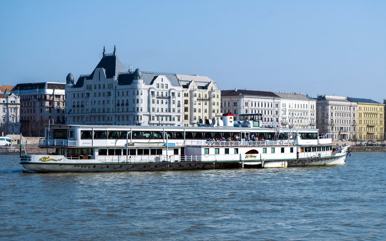 Cruise boat on the Danube River with Budapest architecture in the background.