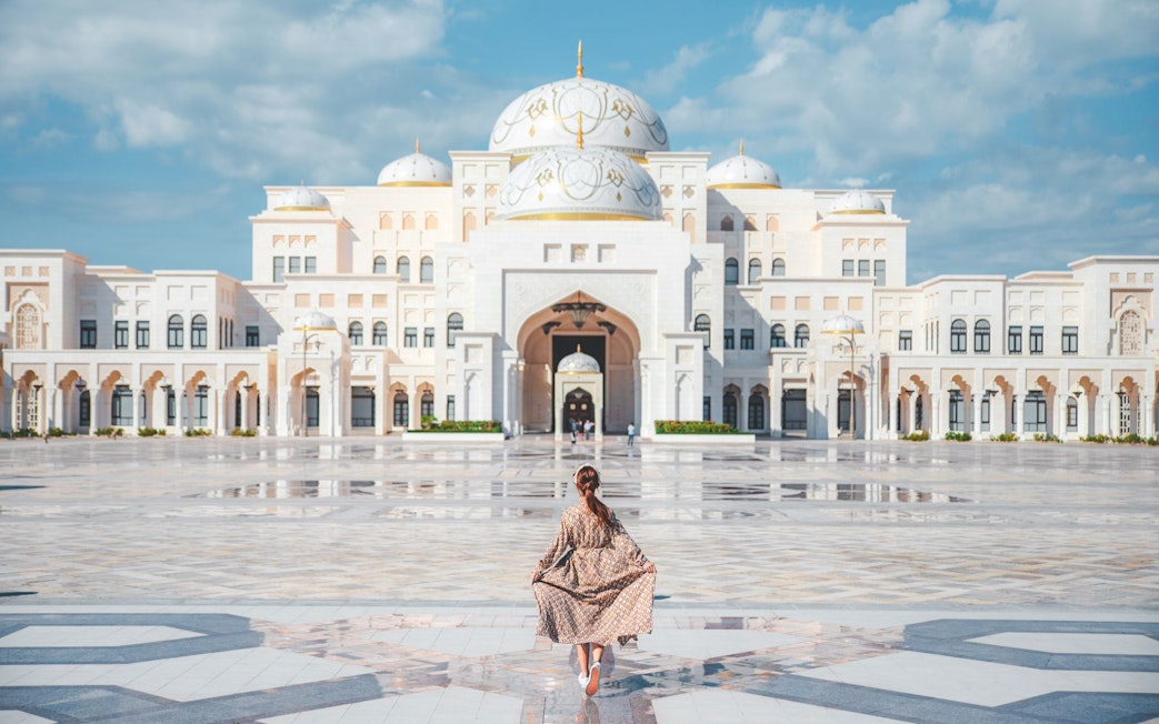 Woman walking towards Qasr Al Watan in Abu Dhabi, showcasing the palace's grand architecture.