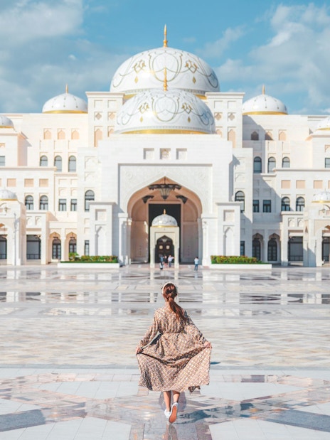 Woman walking towards Qasr Al Watan in Abu Dhabi, showcasing the palace's grand architecture.
