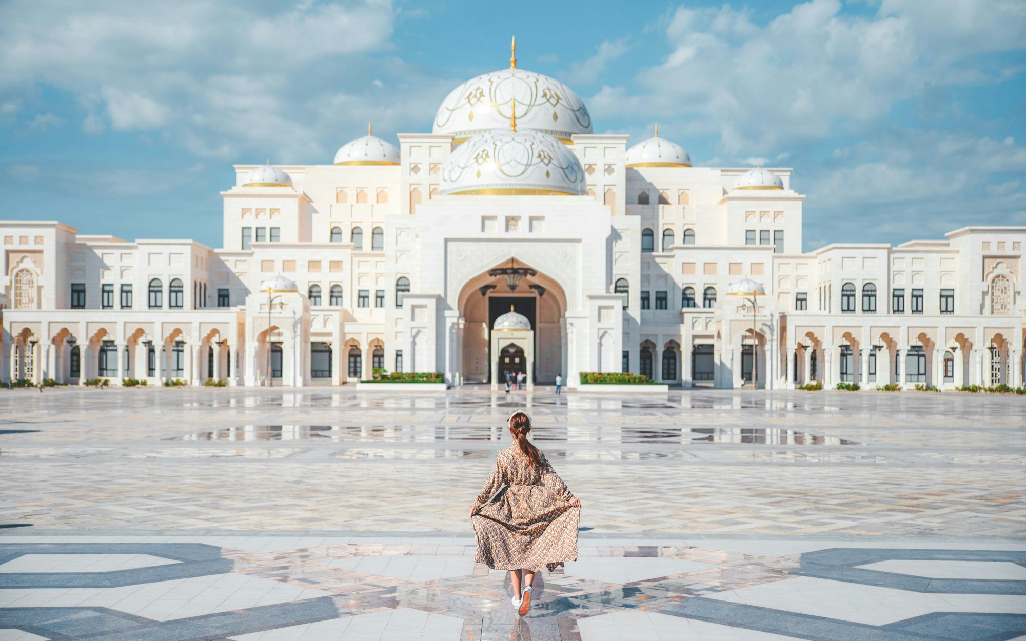 Woman walking towards Qasr Al Watan in Abu Dhabi, showcasing the palace's grand architecture.