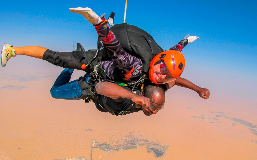 Tandem skydivers freefalling over Dubai desert with clear blue sky.