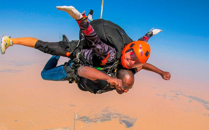 Tandem skydivers freefalling over Dubai desert with clear blue sky.