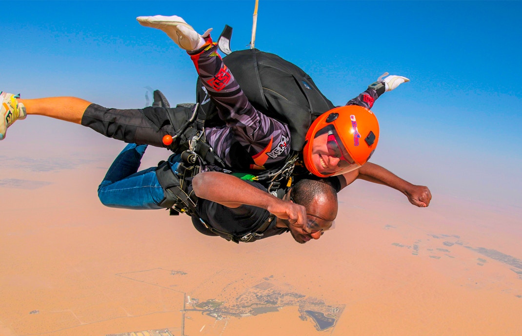 Tandem skydivers freefalling over Dubai desert with clear blue sky.
