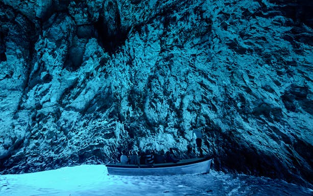 Boat entering Blue Cave, Adriatic Sea, Croatia, with sunlight illuminating the cave's vibrant blue waters.