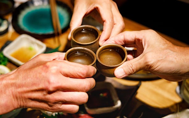 Three hands toasting with sake cups at a Japanese dining table.
