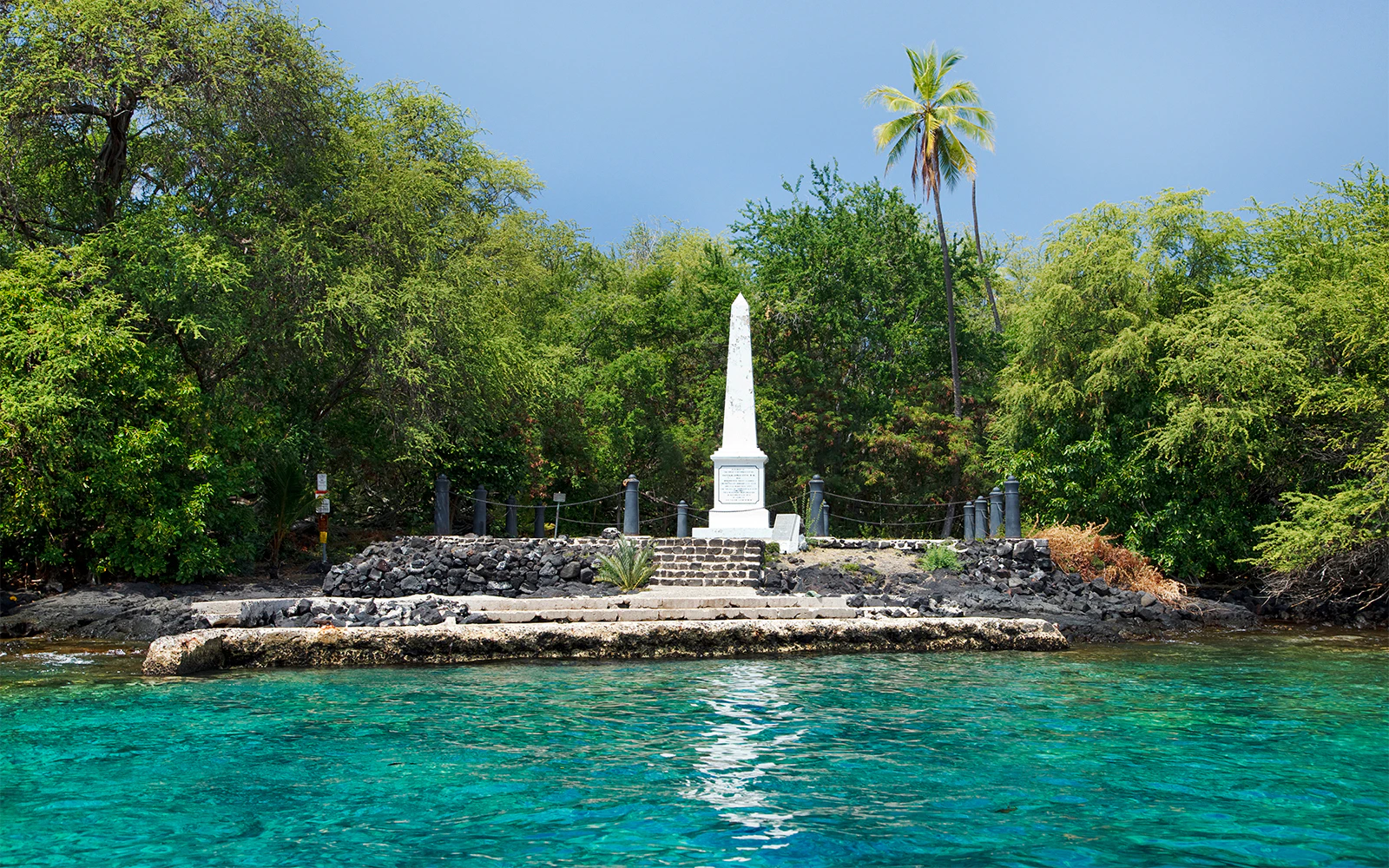 Captain Cook Monument at Kealakekua Bay, Hawaii surrounded by lush greenery and clear blue water.