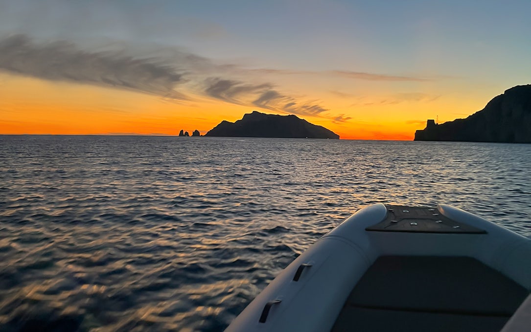 Sunset view from a boat on the Amalfi Coast with distant silhouette of cliffs.