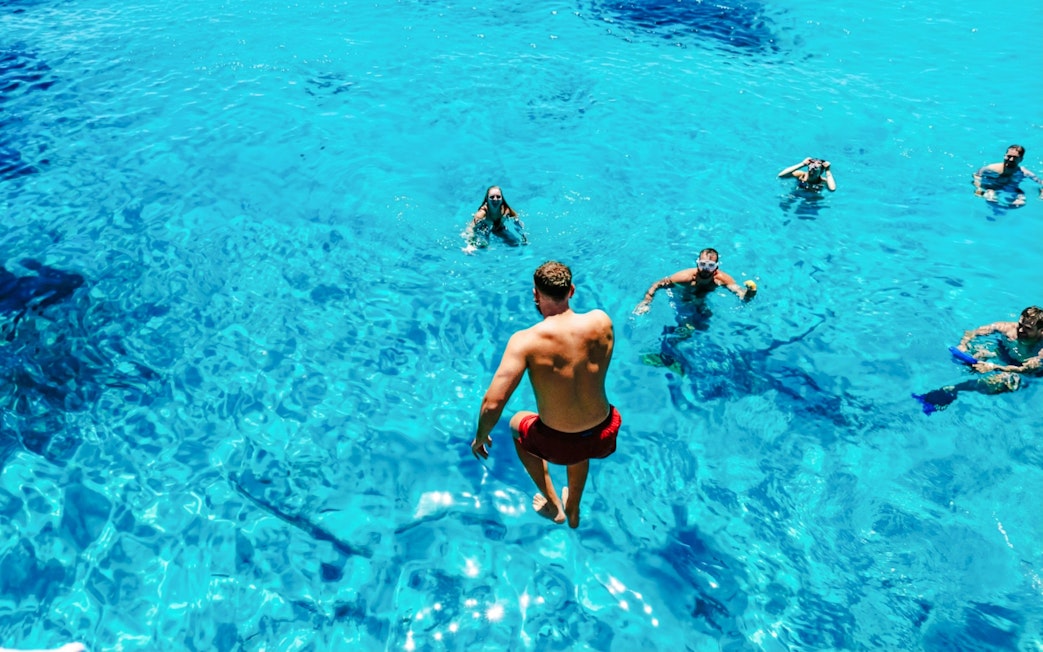 People swimming in clear blue waters during a motorboat tour of the La Maddalena Archipelago.