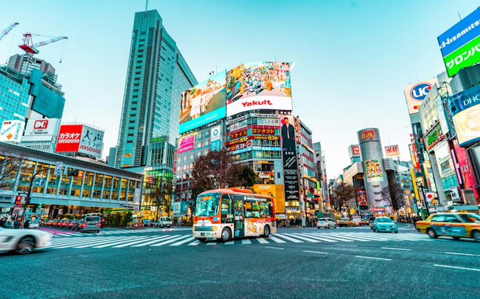 Shibuya Crossing in Tokyo with colorful billboards and a bus during the guided walking tour.