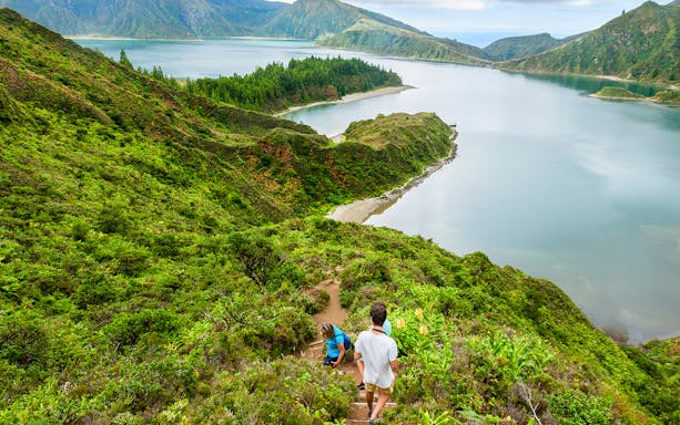 Hikers descending a lush trail towards Lagoa do Fogo in the Azores.