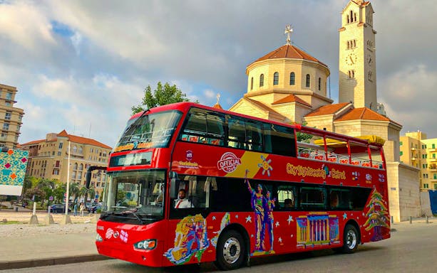Red double-decker bus for Beirut Hop On Hop Off tour near a historic church.