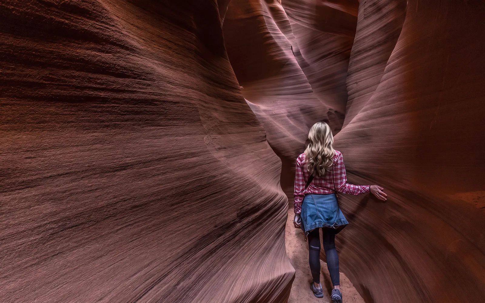 Visitor exploring narrow sandstone passage in Secret Antelope Canyon tour.