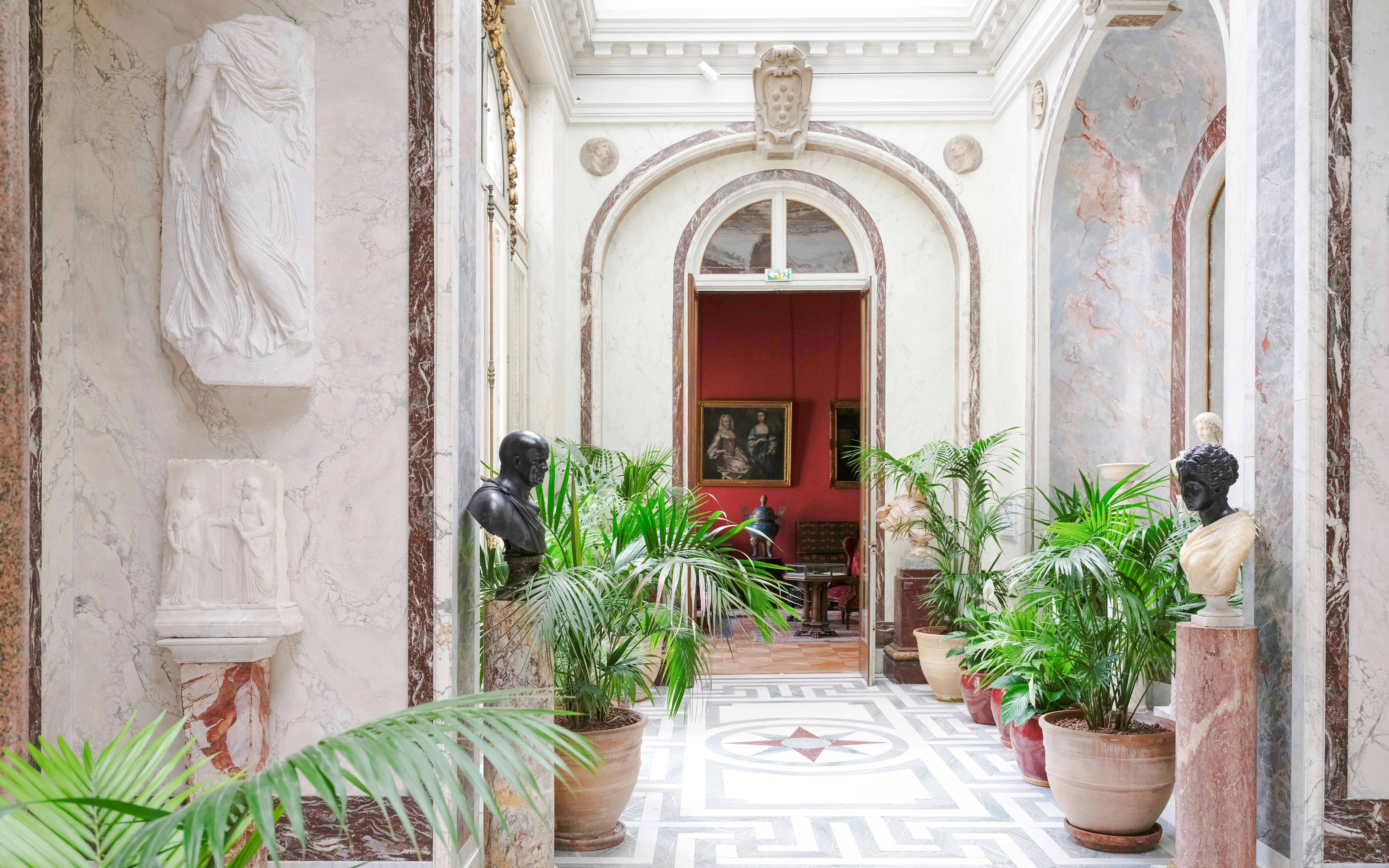 Jacquemart André Museum corridor with sculptures and potted plants.