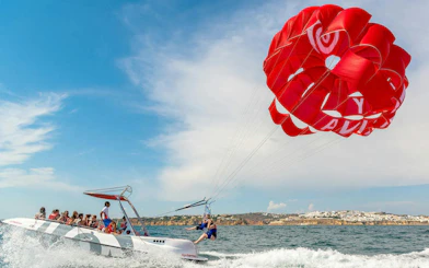 Parasailing adventure over the ocean in Albufeira with a red parachute.