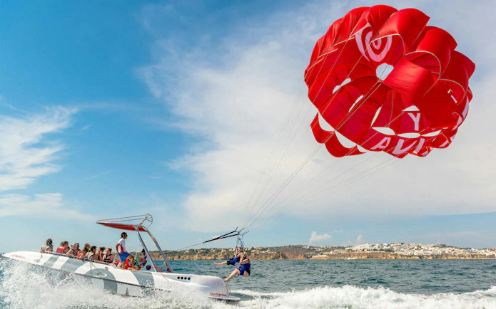 Parasailing adventure over the ocean in Albufeira with a red parachute.