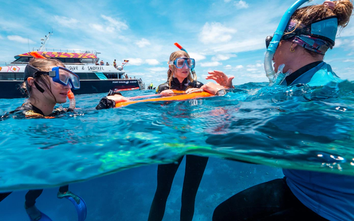 Snorkelers in Cairns exploring outer reefs with a dive boat in the background.