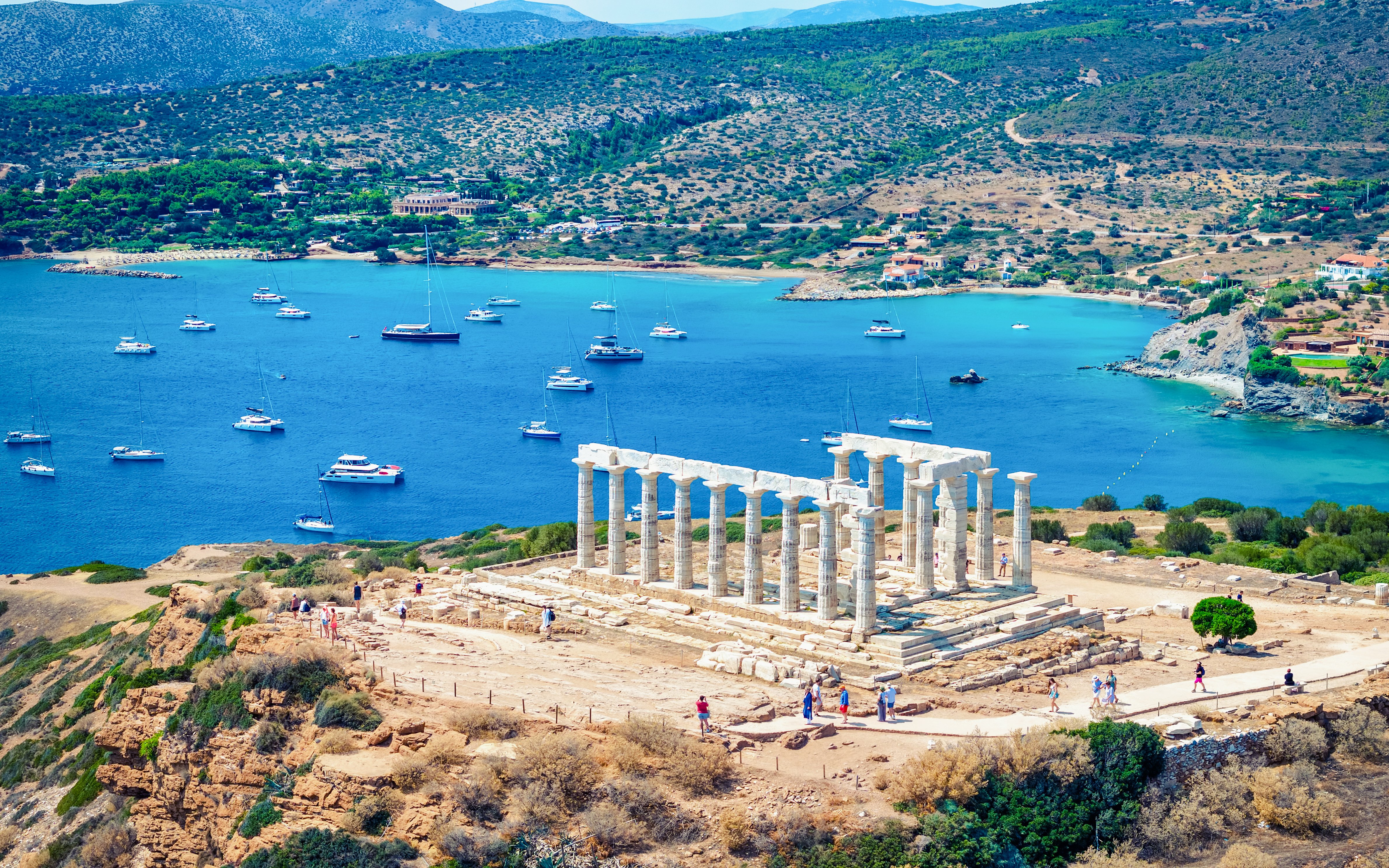 Temple of Poseidon overlooking the Aegean Sea with boats in Sounion, Greece.