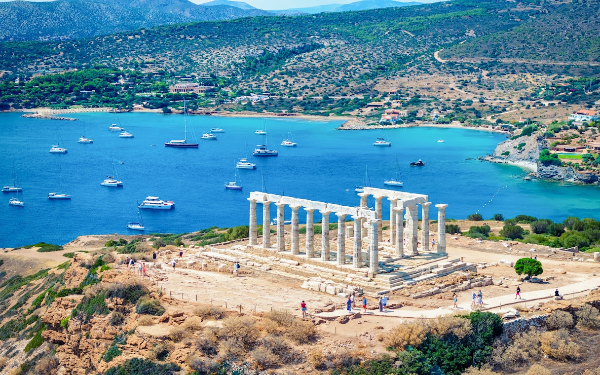 Temple of Poseidon overlooking the Aegean Sea with boats in Sounion, Greece.