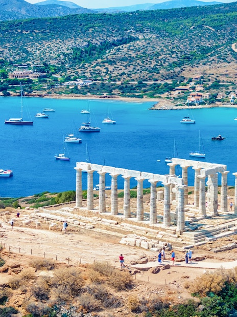 Temple of Poseidon overlooking the Aegean Sea with boats in Sounion, Greece.