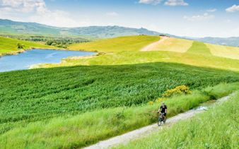 Cyclist on e-bike tour through Tuscany countryside with rolling hills and a lake.