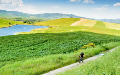Cyclist on e-bike tour through Tuscany countryside with rolling hills and a lake.